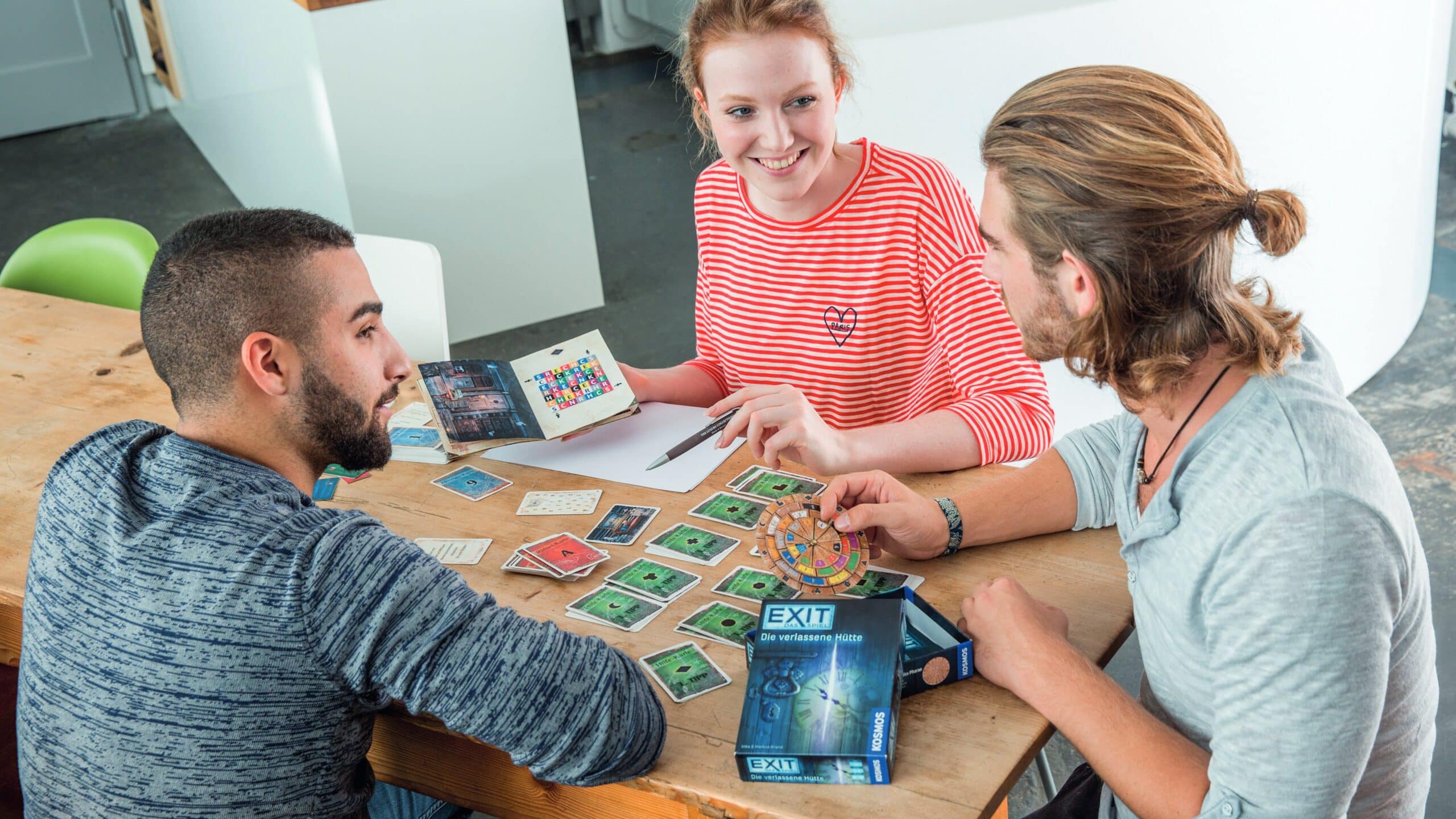 Three friends sit at a table and play the EXIT game The Abandoned Cabin.