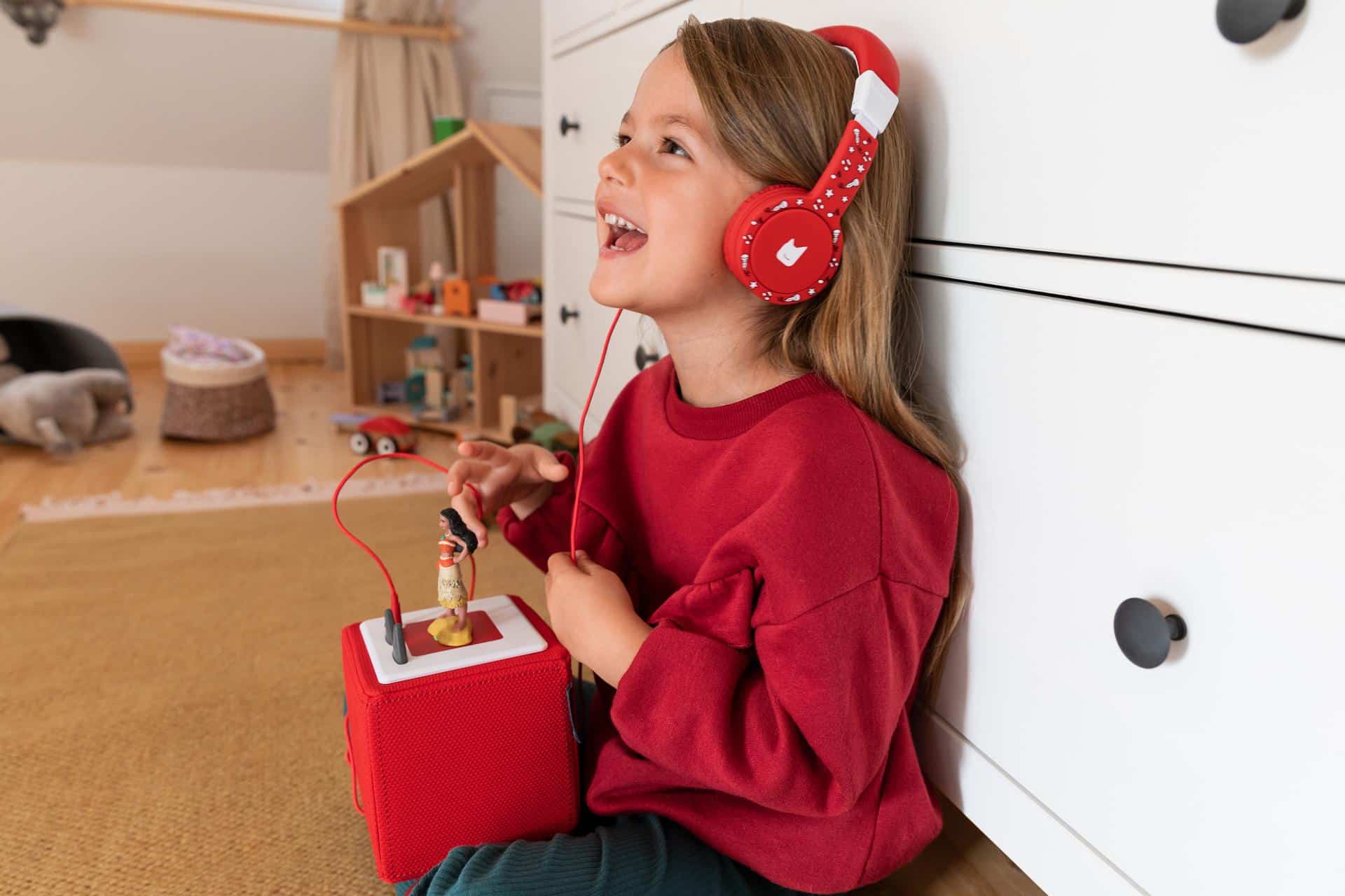A girl sits in her room and listens to music on her Toniebox via headphones.